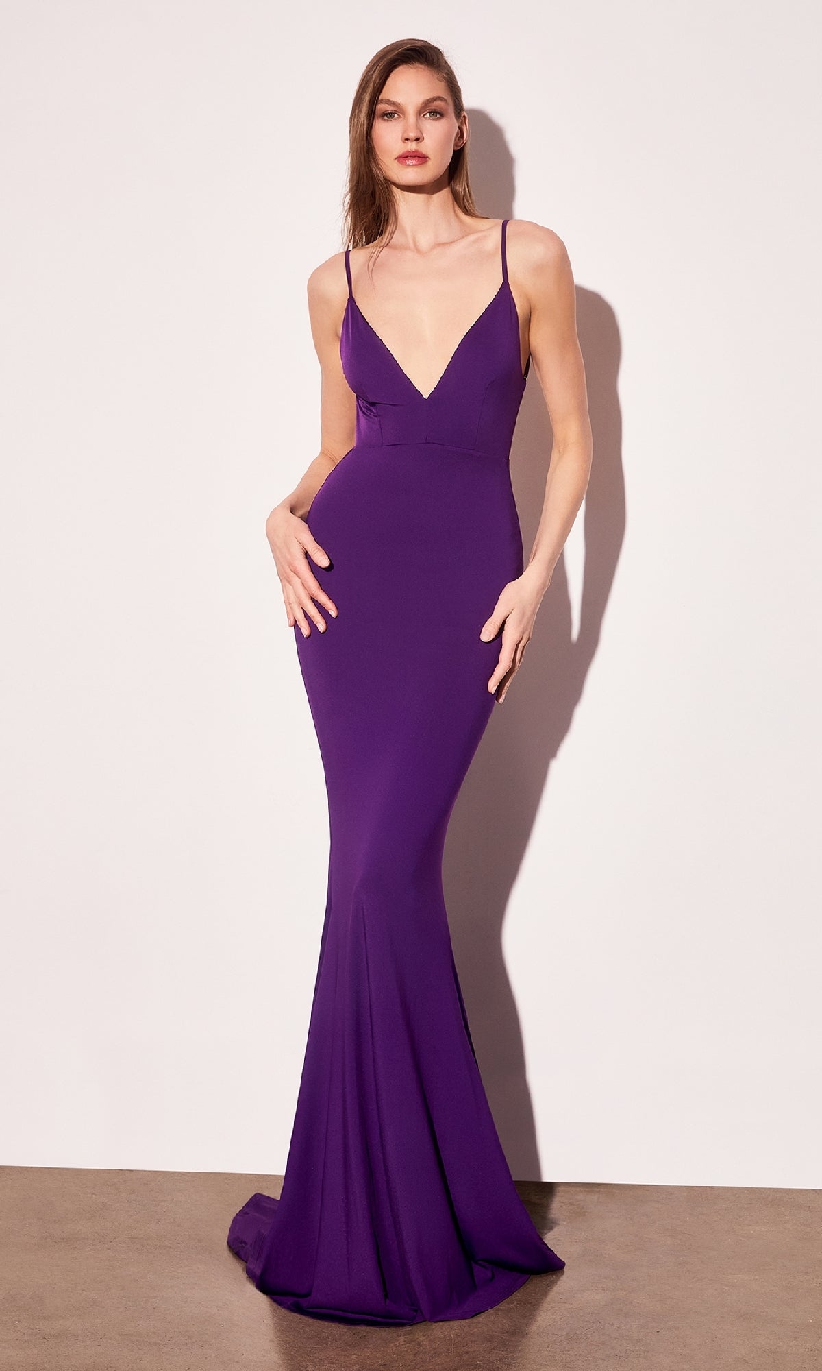 A woman poses against a plain background in the Open-Back Long Bodycon Prom Dress: Astee T905, a floor-length, sleeveless gown with a fitted bodice, flared hem, and deep violet color—ideal for formal events.